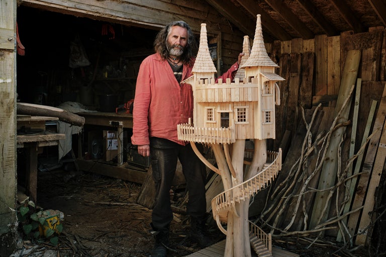 Mann steht neben einem Holzbaumhausmodell in einer Werkstatt