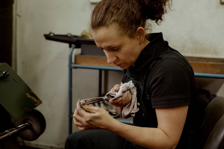 Une femme polit un produit métallique avec un chiffon dans un atelier.