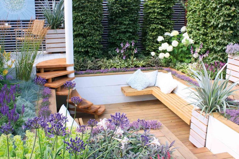 Gestalteter Gartenbereich mit Holzterrasse, Sitzbank und bepflanzten Beeten.