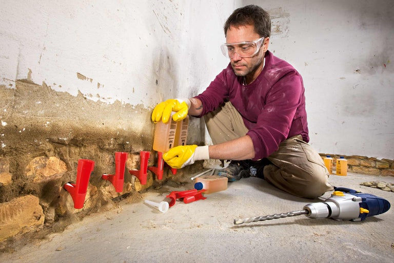 Artisan injectant une barrière horizontale dans un mur pour réparer les dégâts causés par l'humidité