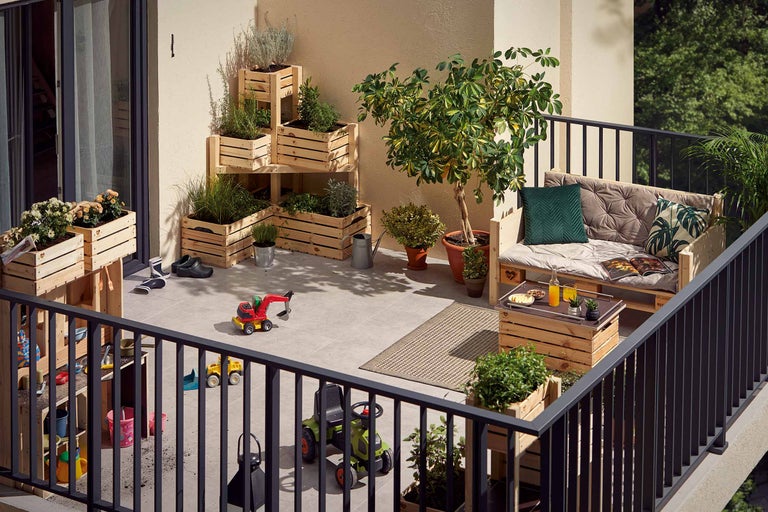 Balkon mit Holzmöbeln, Pflanzen in Holzkisten, Kinderspielzeug und Teppich