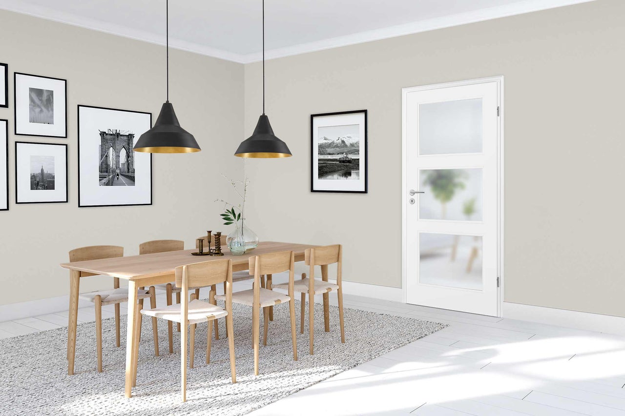 Salle à manger lumineuse avec table en bois, chaises et porte intérieure blanche avec inserts en verre.