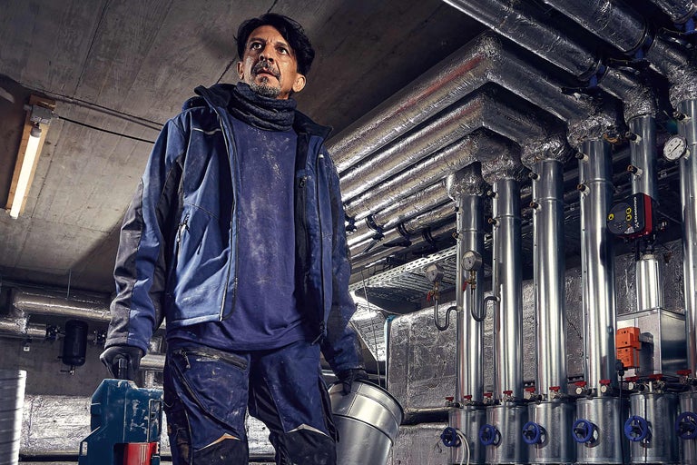 Un installateur avec une cuve métallique devant des tuyaux de chauffage dans une cave.