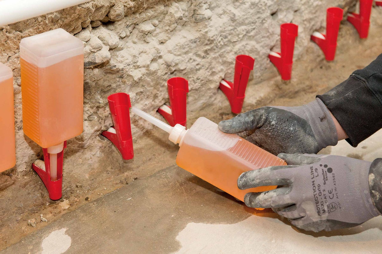 Gros plan de canules d'injection remplies de liquide, fixées dans un mur, tandis qu'une personne portant des gants de protection remplit une autre canule