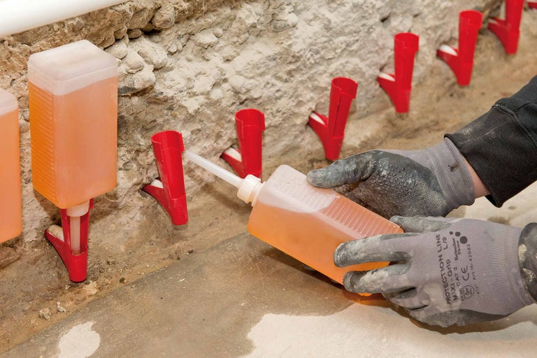 Gros plan de canules d'injection remplies de liquide, fixées dans un mur, tandis qu'une personne portant des gants de protection remplit une autre canule