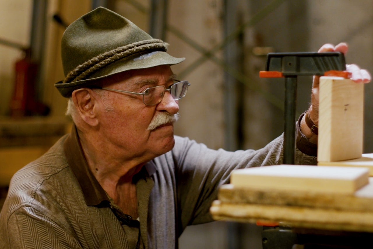 Un homme coiffé d'un chapeau fixe des morceaux de bois avec un serre-joint.
