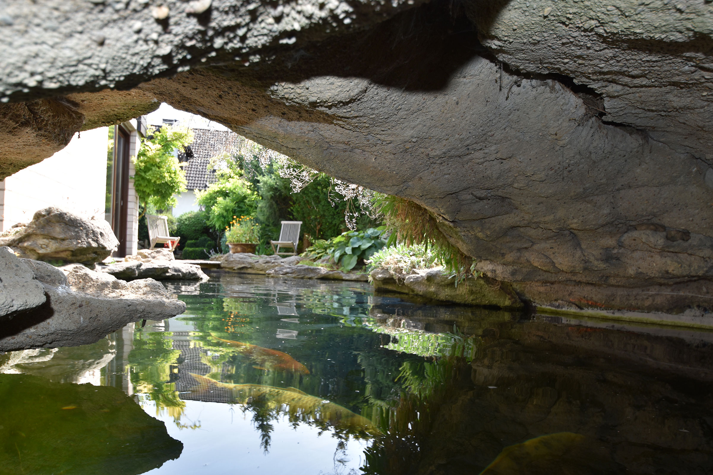 Teich mit Felsen und Gartenmöbeln im Hintergrund