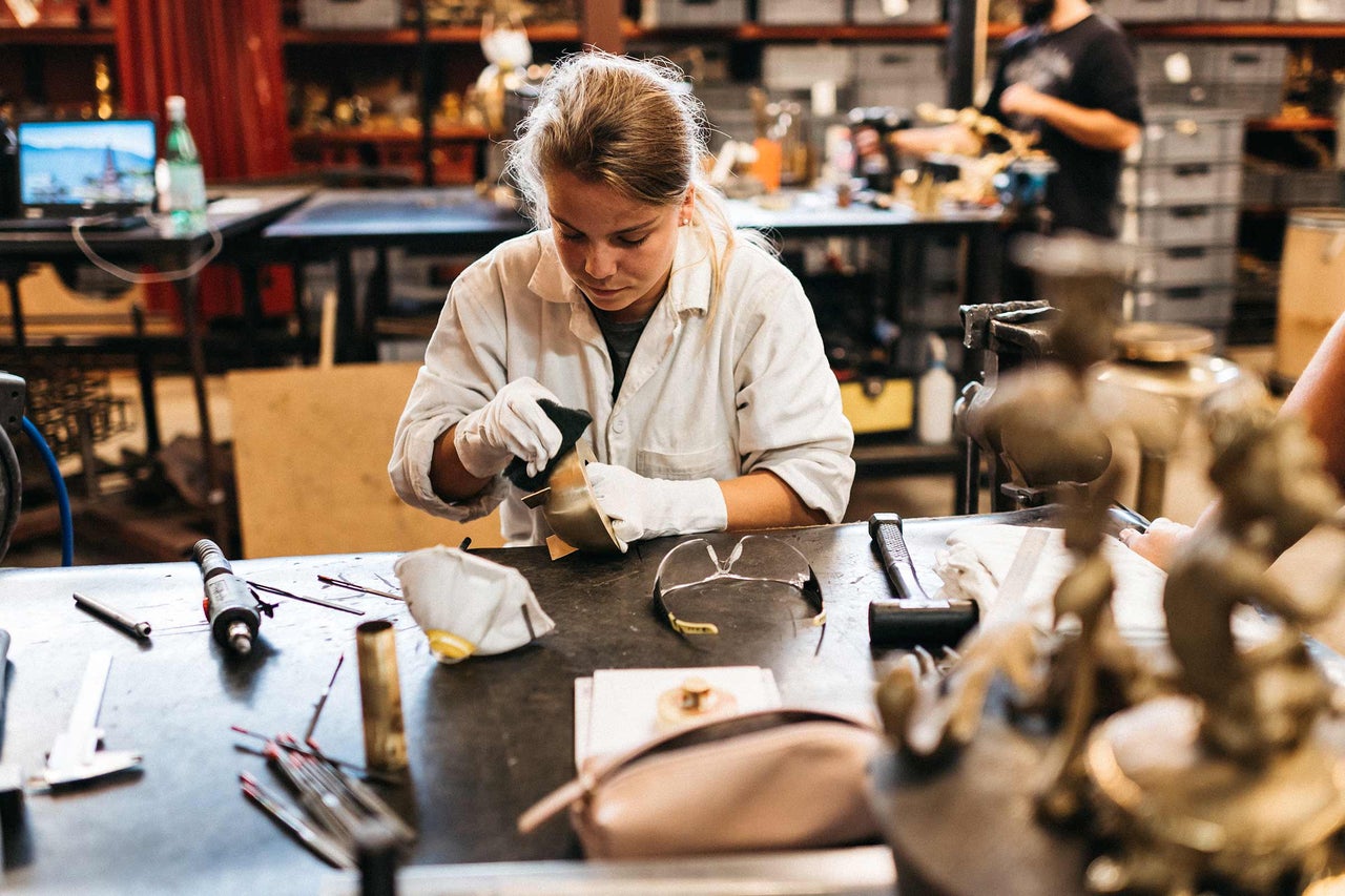 Femme polissant un objet métallique avec des outils sur un établi