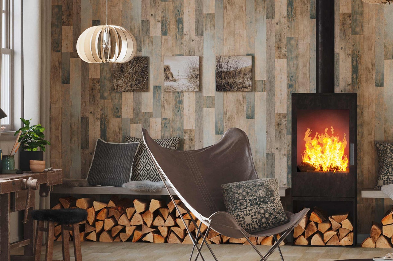 Salon avec cheminée, fauteuil, tas de bois et panneaux muraux aspect bois pour une ambiance chaleureuse