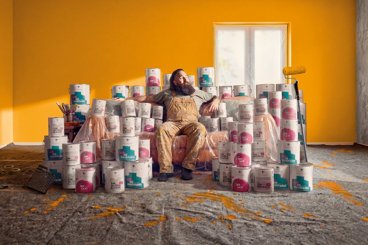 Un homme en vêtements de travail peints se détend sur une pile de boîtes de peinture dans une pièce peinte en jaune.