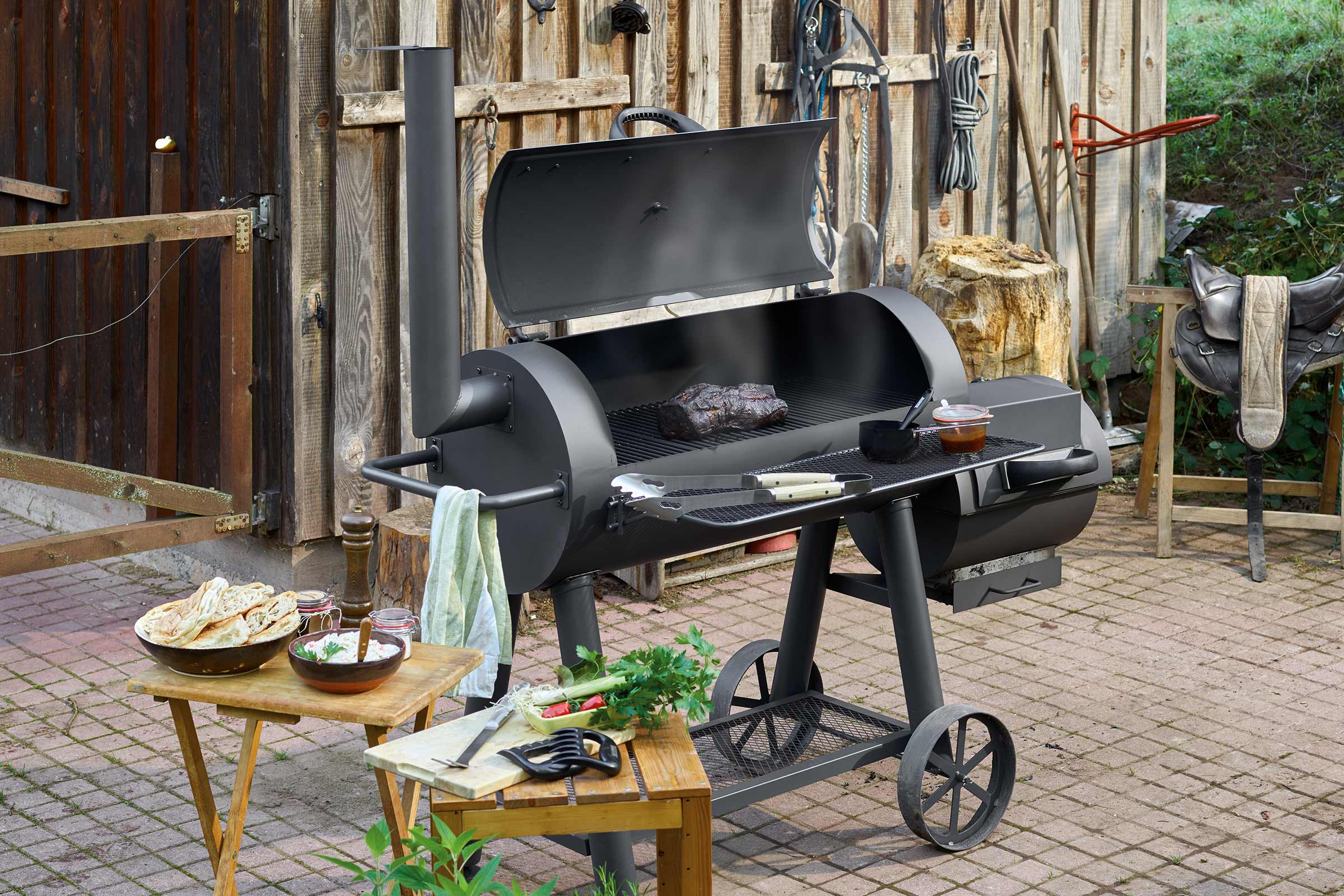 Grill fumoir noir avec des aliments grillés et des accompagnements dans le jardin.
