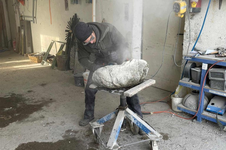 Steinmetz bearbeitet einen Stein mit einem Winkelschleifer in einer Werkstatt