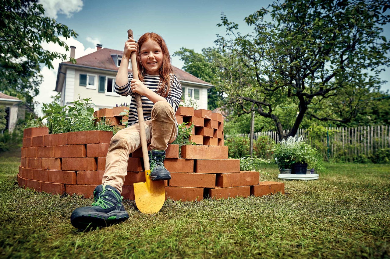 Une fille est assise avec une bêche sur un mur en briques dans le jardin.