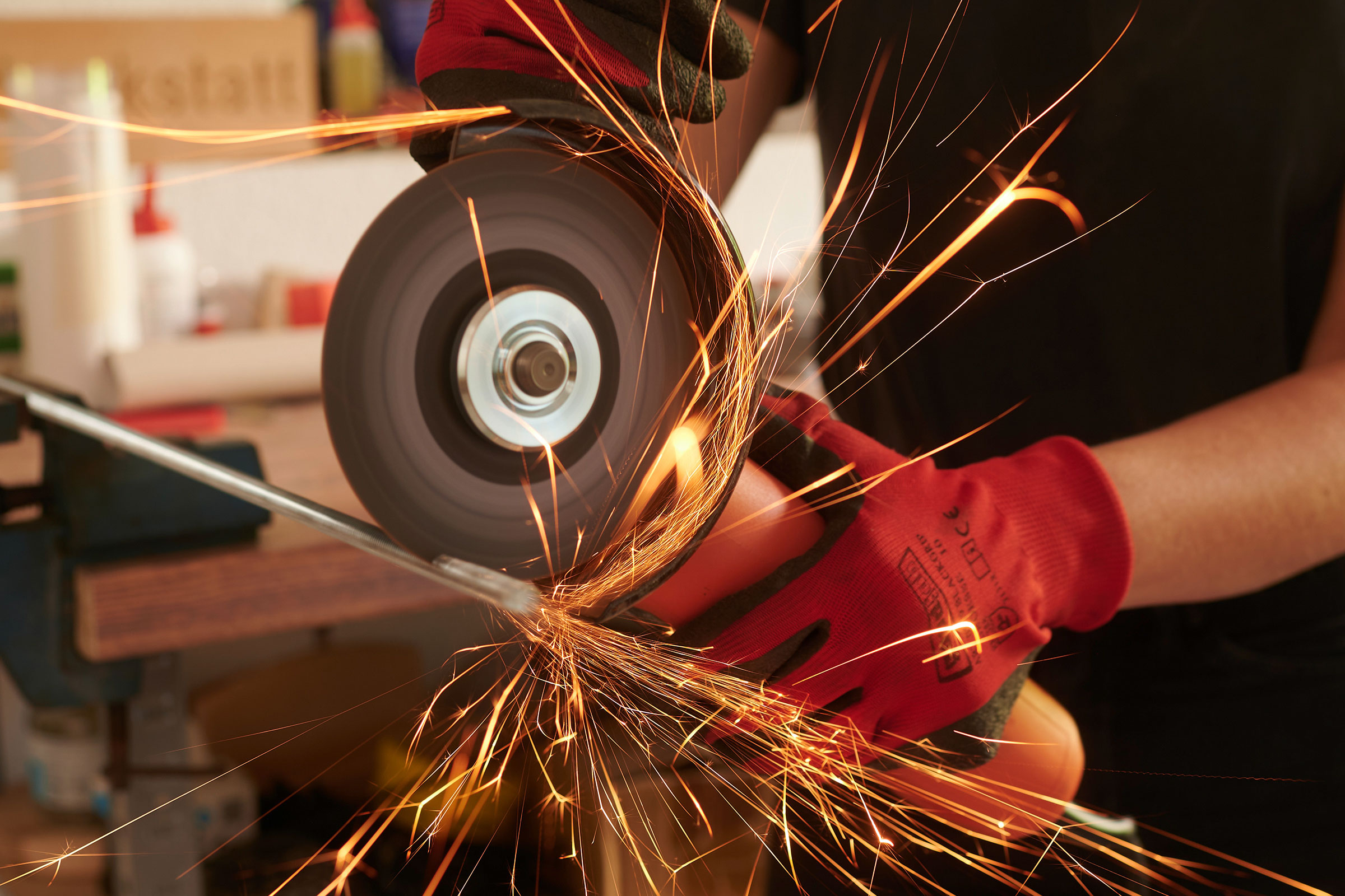 Nahaufnahme einer Person, die mit einem Winkelschleifer Metall schleift, wobei Funken fliegen