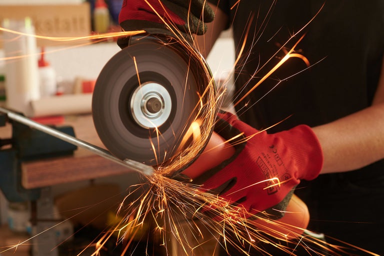 Gros plan d'une personne utilisant une meuleuse d'angle pour meuler du métal, avec des étincelles qui volent