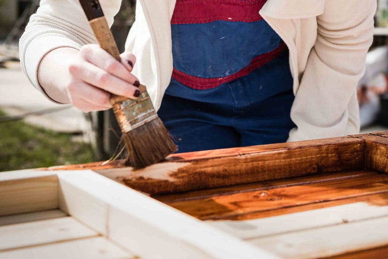 Person streicht Holzrahmen mit Pinsel und Holzschutzlasur