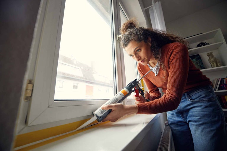 Frau dichtet Fenster mit Dichtmasse ab