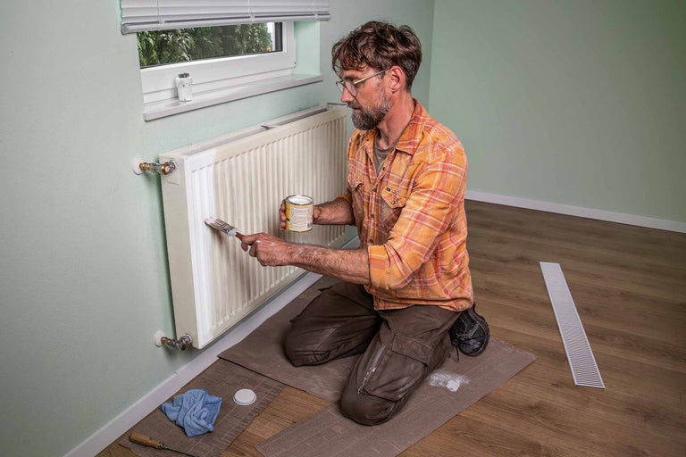 Un homme peint un radiateur avec un pinceau et de la peinture.