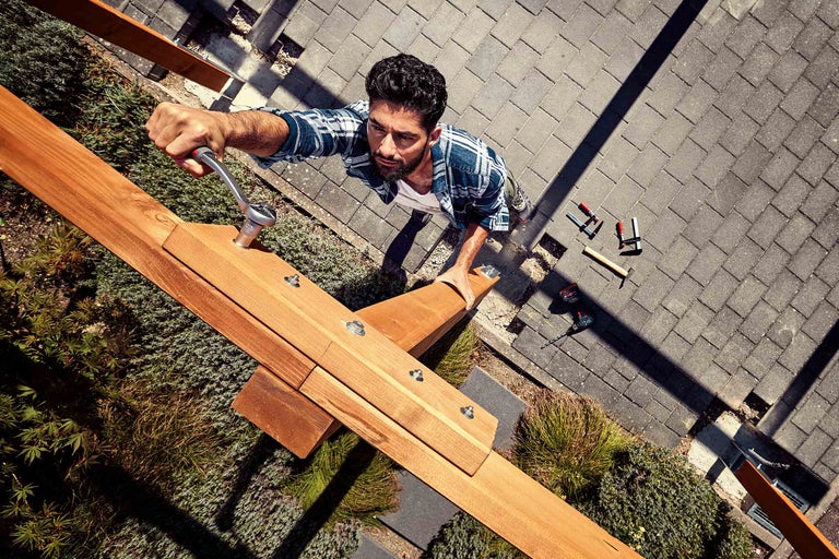 Un homme fixe une construction en bois dans le jardin avec une clé à molette