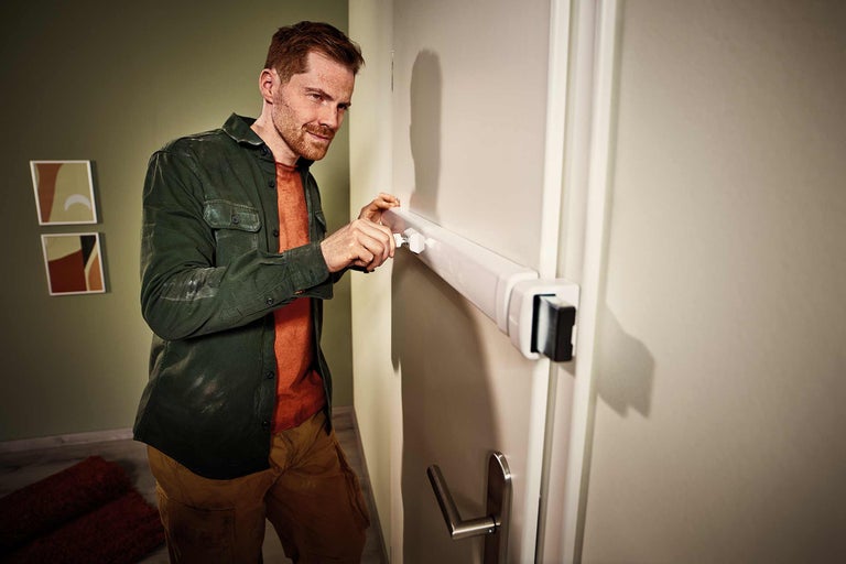 Un homme installe un interphone de porte blanc sur une porte