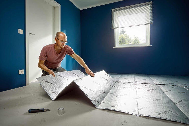 Un homme pose une sous-couche isolante Twinfoam sur un sol en préparation d'un nouveau revêtement de sol.