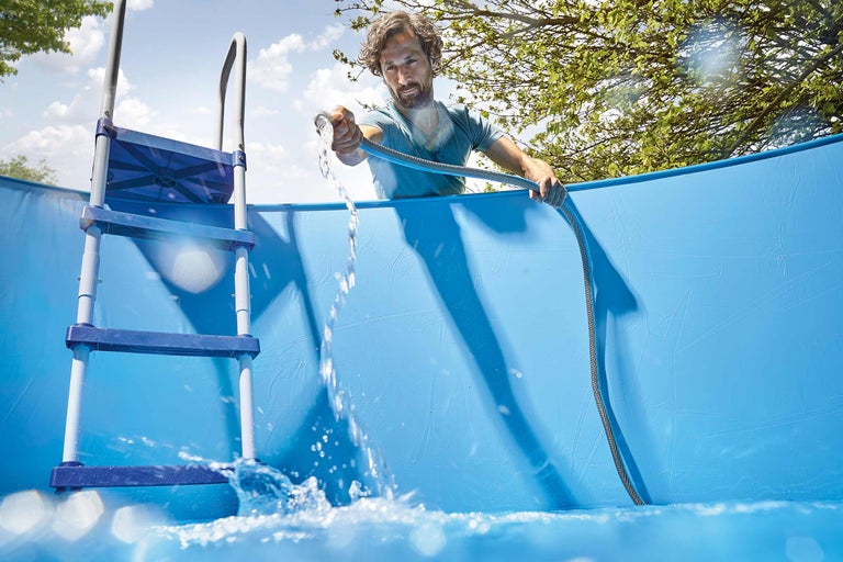 Homme remplissant une piscine hors sol avec un tuyau d'arrosage et une échelle