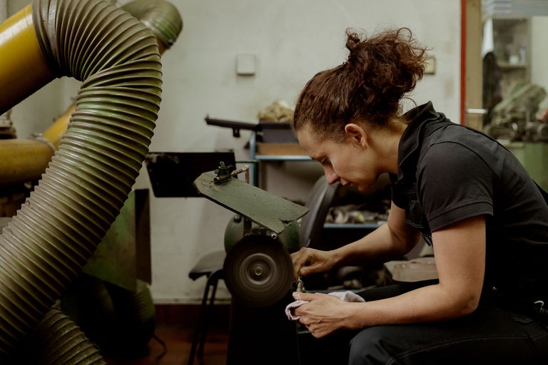 Eine Frau poliert ein Werkstück an einer Poliermaschine. Im Hintergrund befindet sich eine Absauganlage.