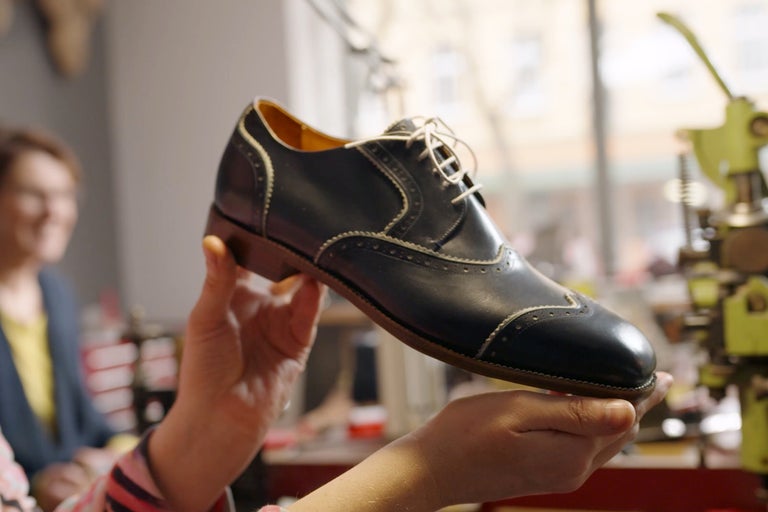 Blauer Lederschuh mit Schnürsenkeln wird in der Hand gehalten