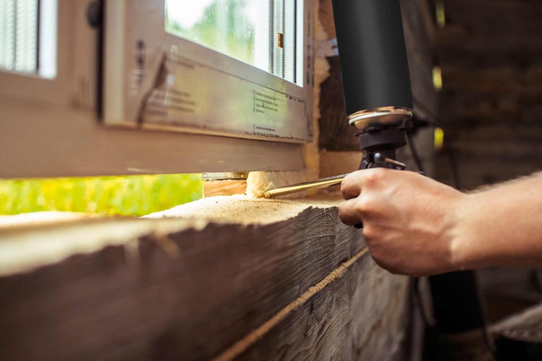 Une main utilise un pistolet à mousse pour isoler une fenêtre.