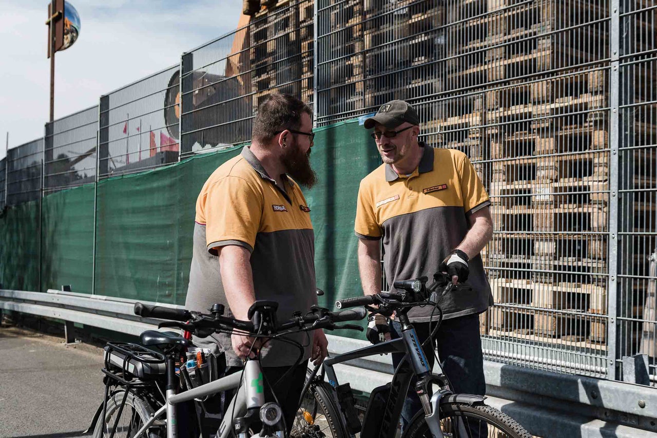Deux employés avec des vélos discutent devant une clôture sur le site Hornbach.