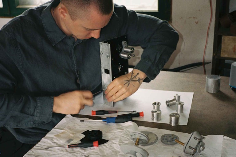 Un artisan assemble un appareil technique sur une table de travail avec des tournevis et divers composants métalliques.