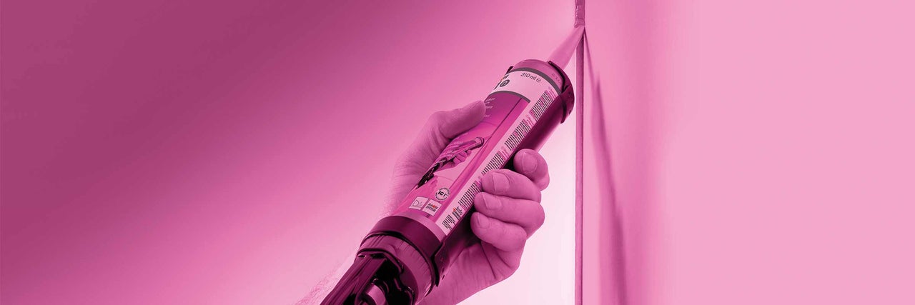 Une main tient une cartouche de mastic contre un coin.