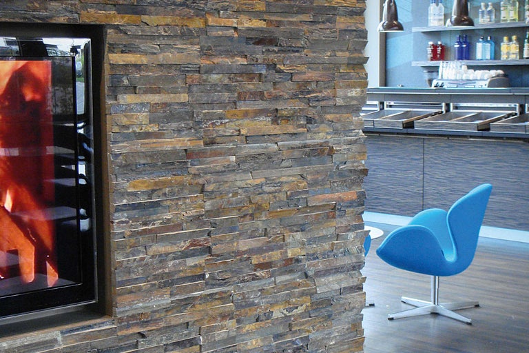 Wandgestaltung mit Natursteinverblendern neben Kamin und blauer Sitzgelegenheit.