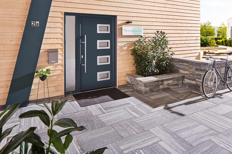 Vue extérieure d'une maison avec mur en bois, porte d'entrée avec fenêtres, boîte aux lettres et pavage en pierre