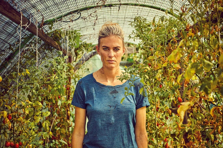 Une femme se tient dans une serre au milieu de plants de tomates.