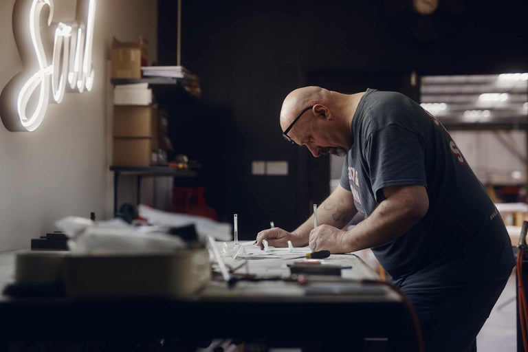 Handwerker bearbeitet Neon Buchstaben auf einer Werkbank