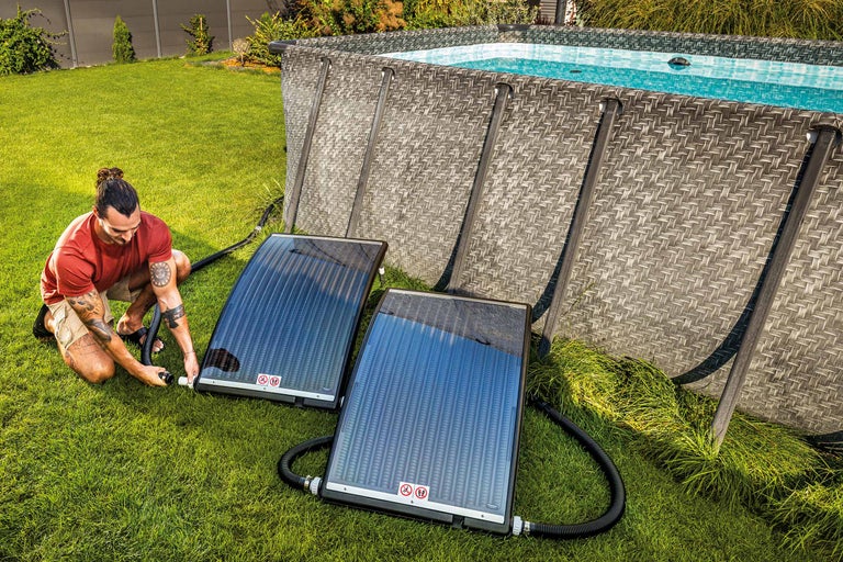 Un homme installe des capteurs solaires à côté d'une piscine de jardin pour chauffer la piscine.