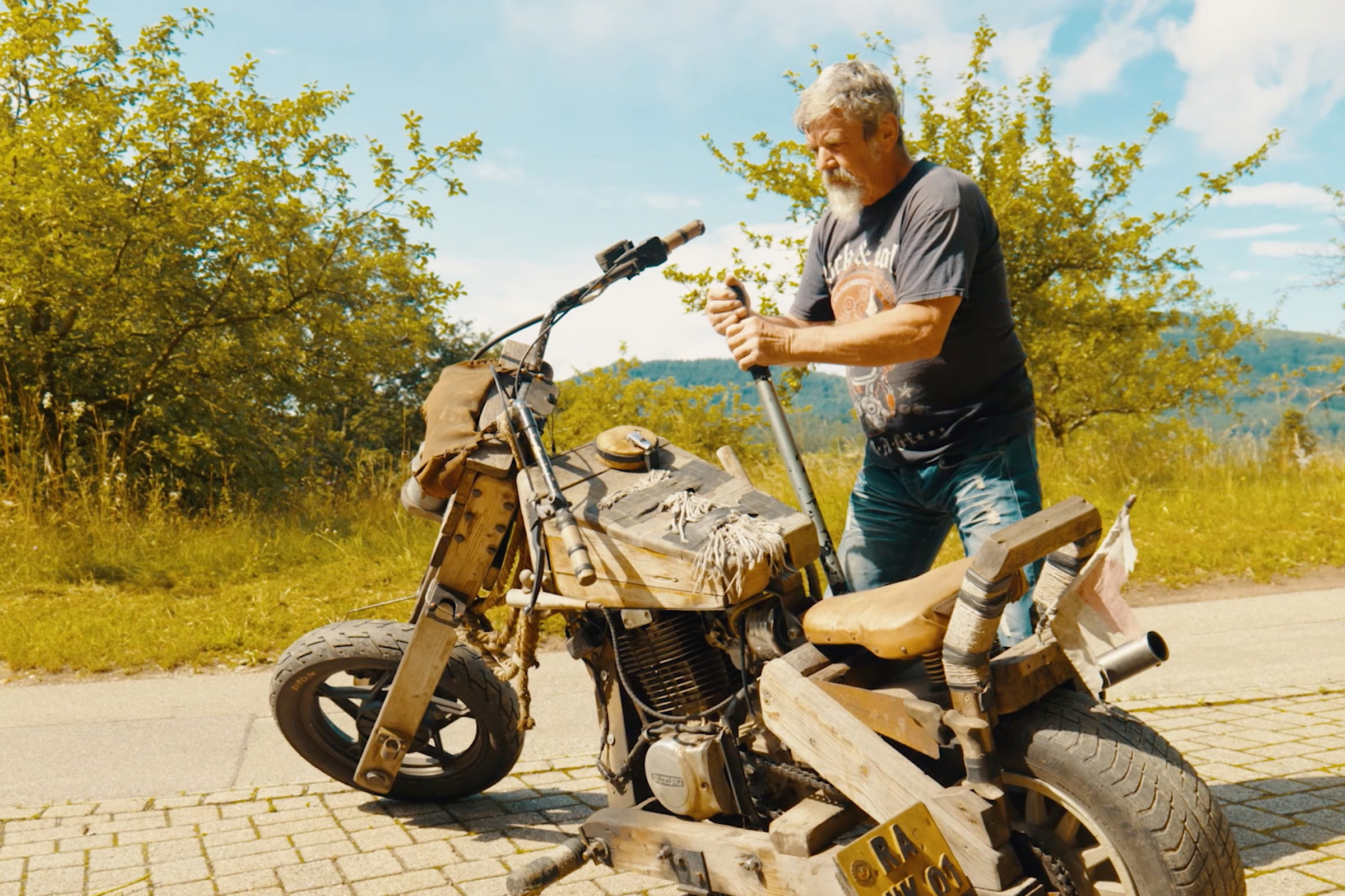 Mann mit Motorrad im Gelände. Das Motorrad ist aus Holz gefertigt.