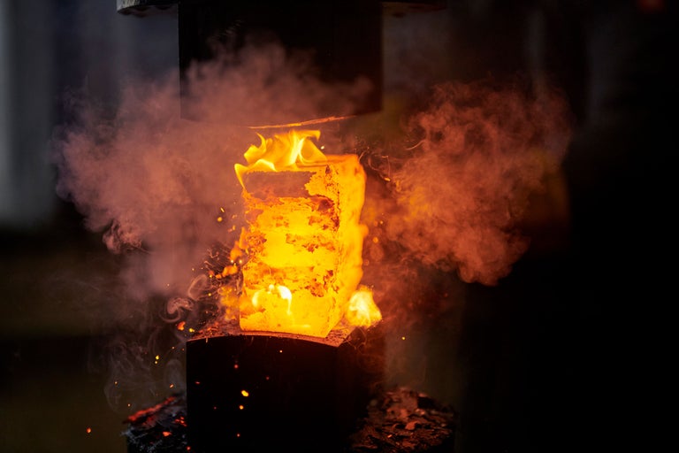 Glühendes Metall wird in einer Schmiedepresse bearbeitet, umgeben von Rauch.