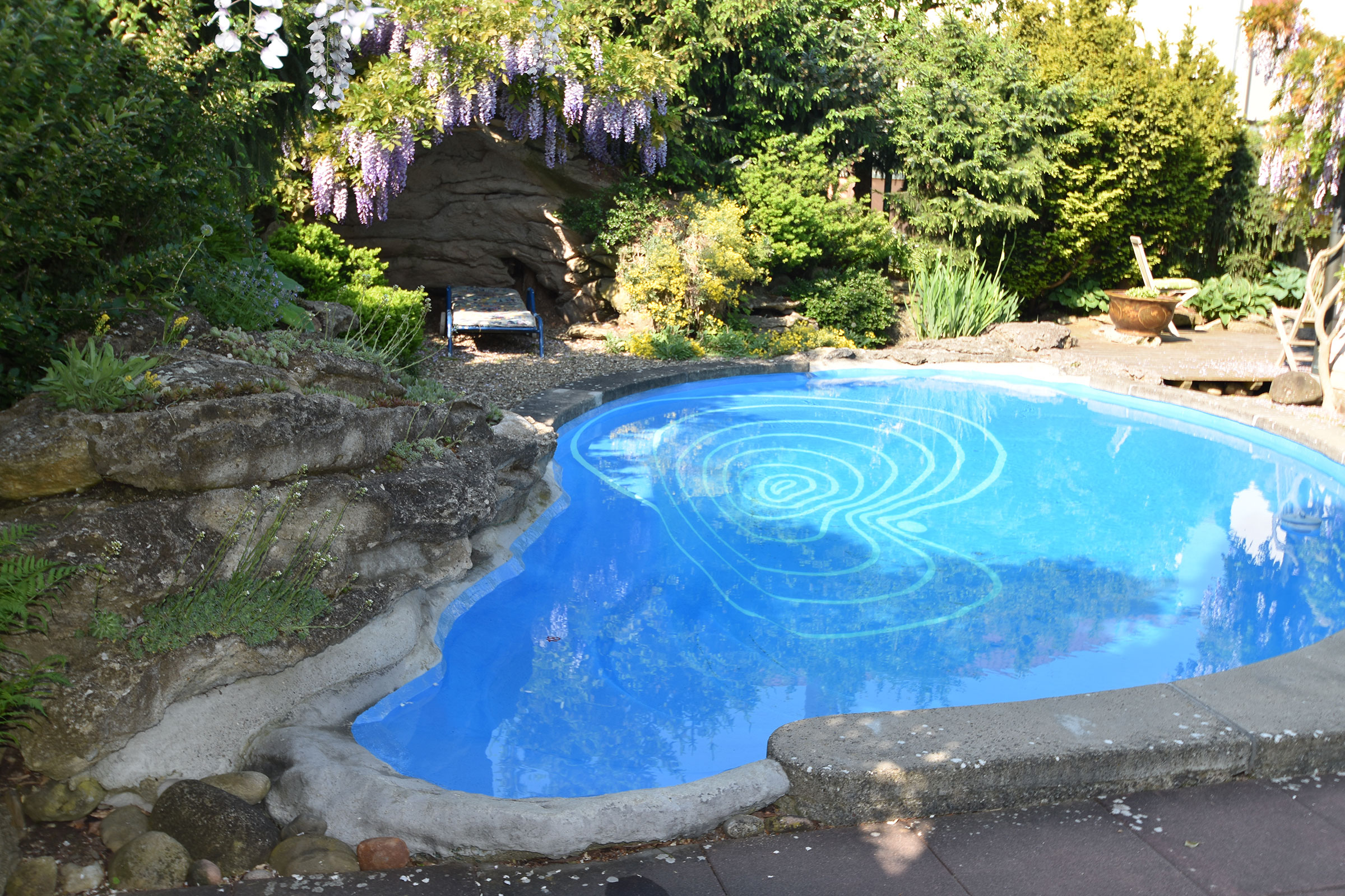 Schwimmbecken im Garten mit blühenden Pflanzen und Steindekoration