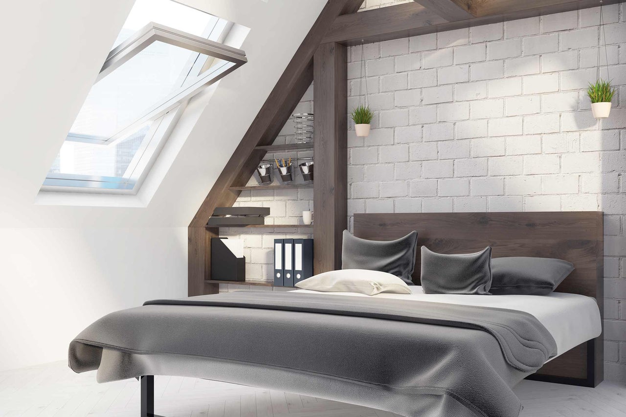 Une chambre dans les combles avec fenêtre de toit, lit, étagère et mur de briques