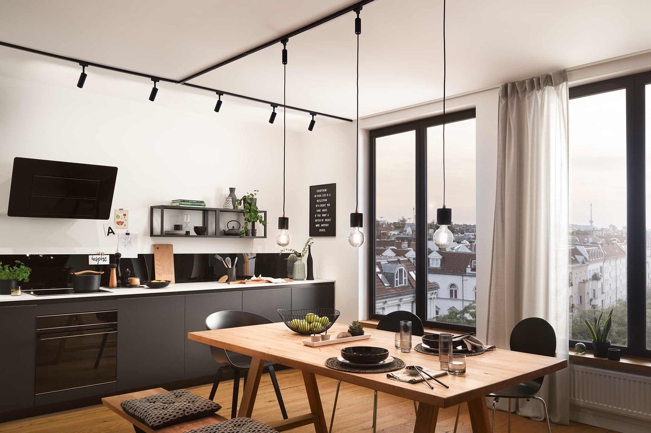 Cuisine claire avec table de salle à manger, kitchenette, suspensions et spots pour montage au plafond.