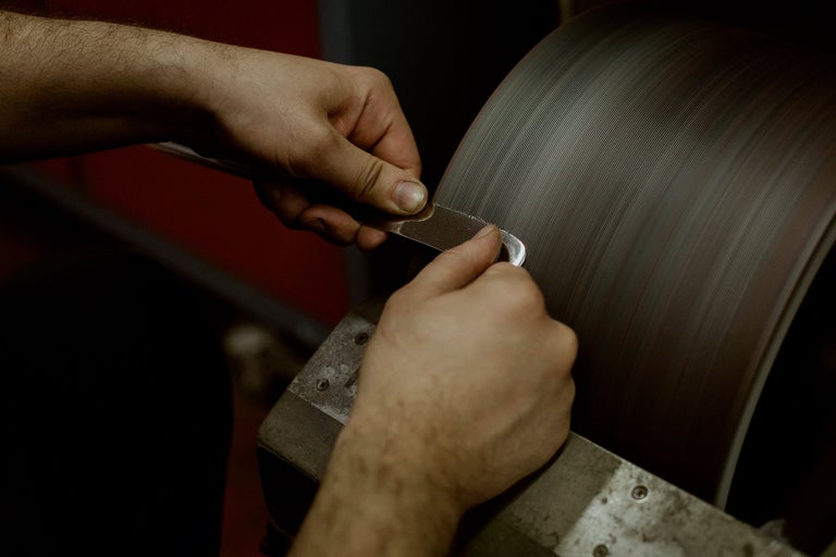 Une personne aiguise un outil sur une meule.