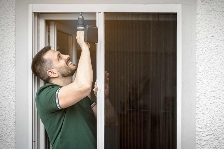 Un homme installe un écran anti-insectes avec un tournevis sans fil sur une fenêtre