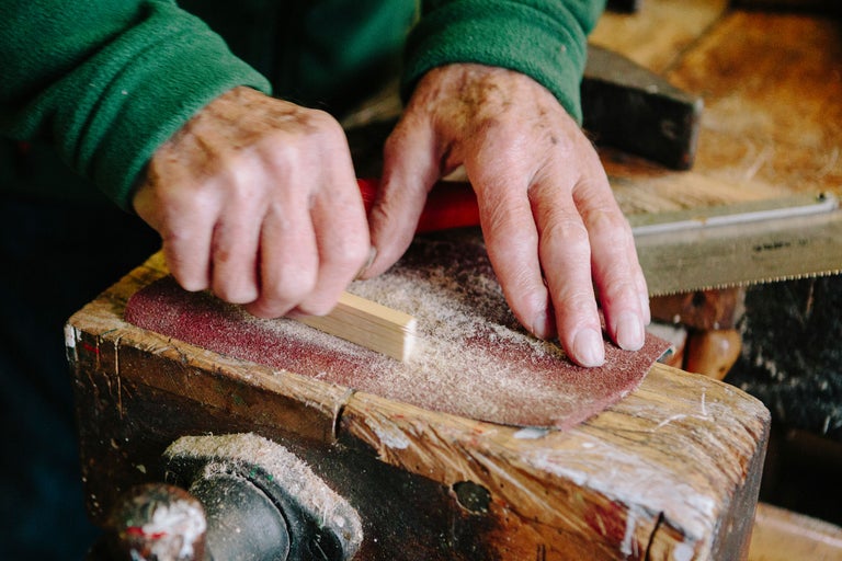 Eine Person schleift ein Holzstück mit Schleifpapier auf einer Werkbank.