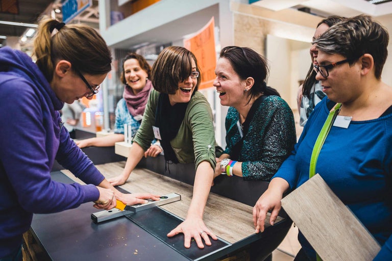 Un groupe de femmes coupe du stratifié avec un cutter et un niveau à bulle sur une table.