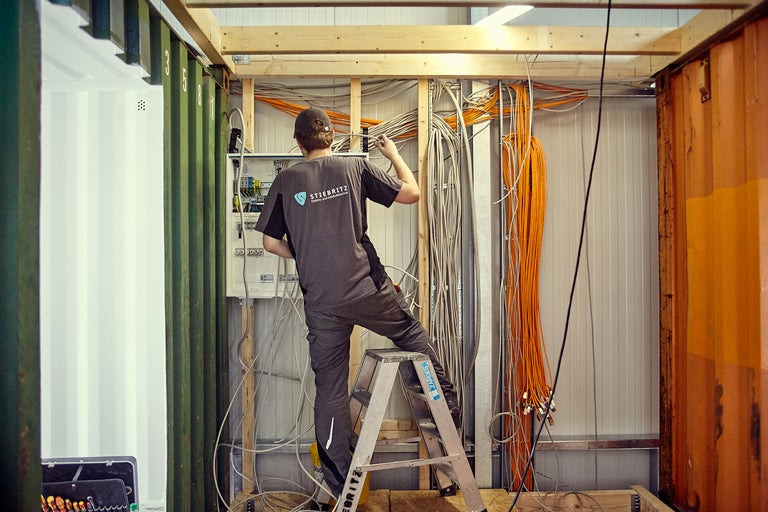 Électricien sur une échelle installant des câbles électriques dans un conteneur