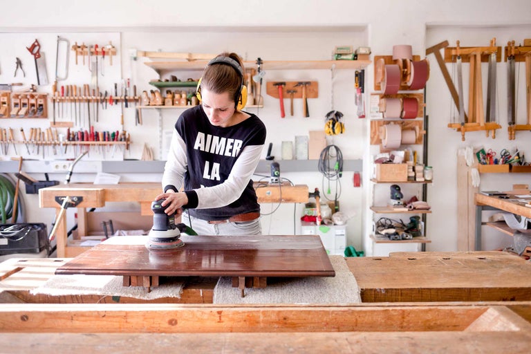 Femme ponçant un plateau de table dans un atelier avec une ponceuse