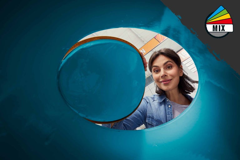 Une femme regarde dans un conteneur à déchets bleu.