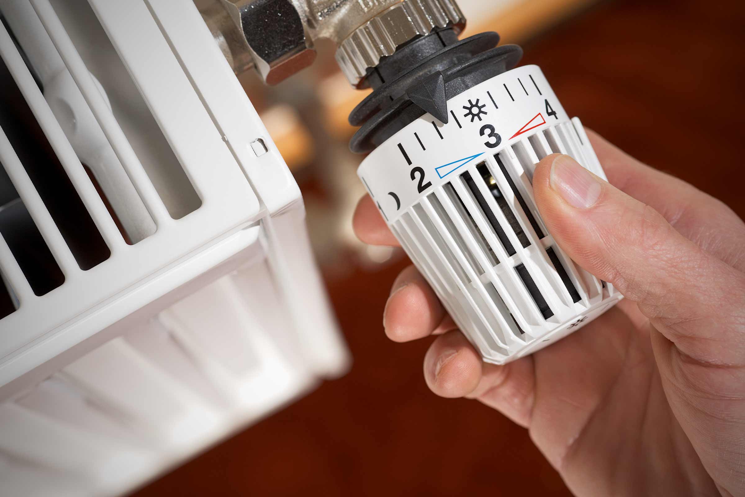 Nahaufnahme eines Heizkörperthermostats, das von einer Hand eingestellt wird